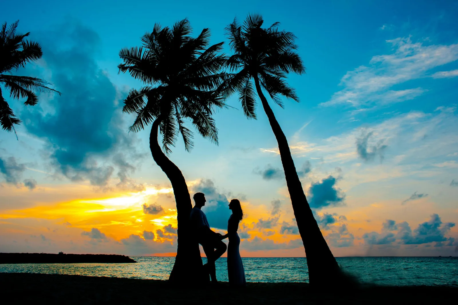 Couple silhouetted beneath palm trees at an Indian Ocean sunset
