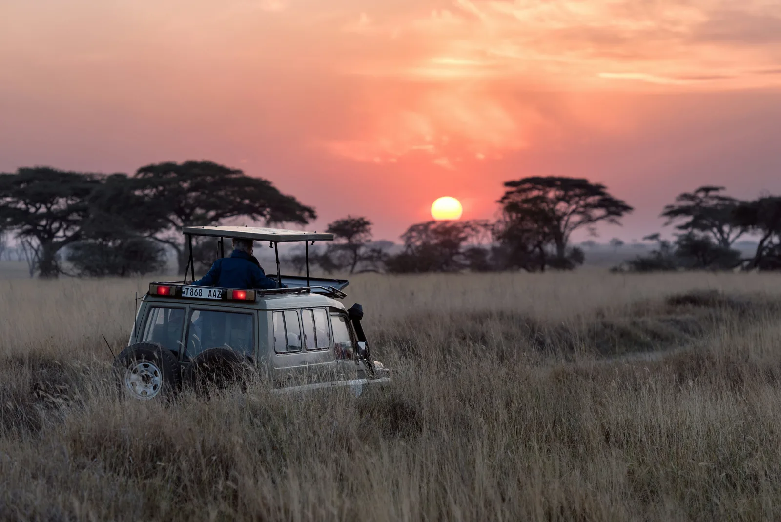 Safari vehicle crossing the Maasai Mara beneath a glowing sunset sky