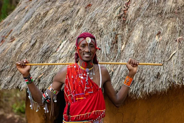 Maasai host standing beside a traditional thatched homestead